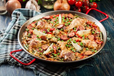 Traditional paella with chicken legs, sausage chorizo and vegetables served in paellera clipart