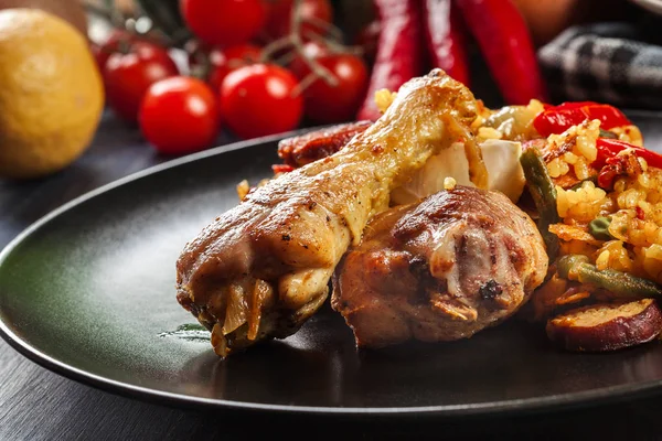 Paella tradicional con patas de pollo, chorizo de salchicha y verduras servidas en plato negro —  Fotos de Stock