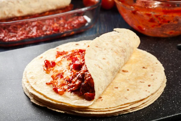 Подготовка традиционных мексиканских энчилад с куриным мясом, острым томатным соусом и сыром — стоковое фото