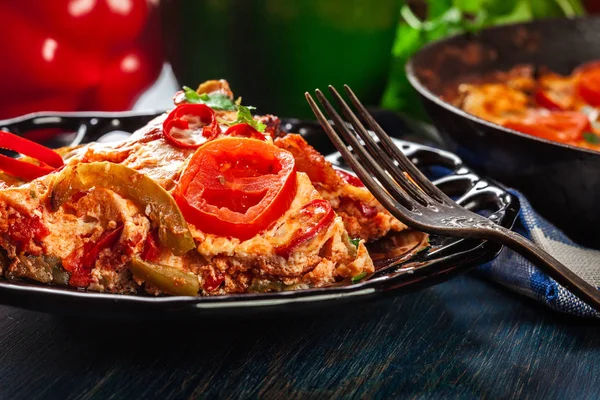 Porción de frittata con huevos, chorizo de salchicha, pimiento rojo, pimiento verde, tomates, queso y chile en un plato sobre mesa de madera . — Foto de Stock