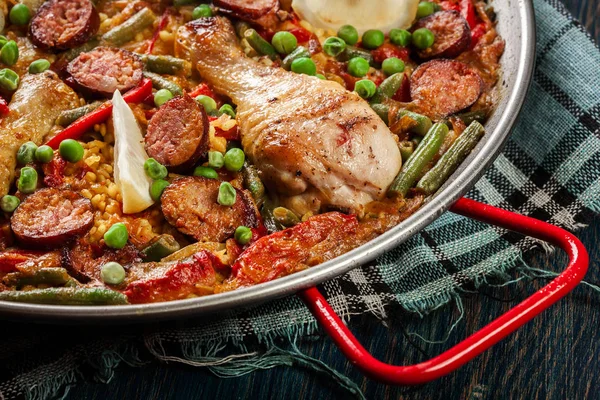 Paella tradicional con patas de pollo, chorizo de salchicha y verduras servida en paellera — Foto de Stock