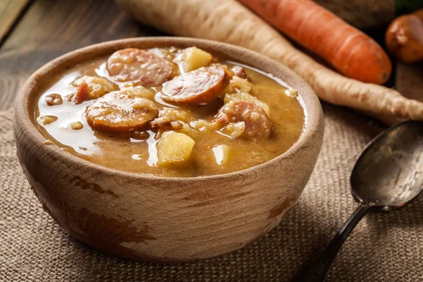 Деревянная тарелка горохового супа с сосисками и картошкой — стоковое фото