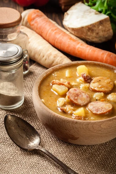 Cuenco de madera de sopa de guisantes partida con salchichas y papas —  Fotos de Stock