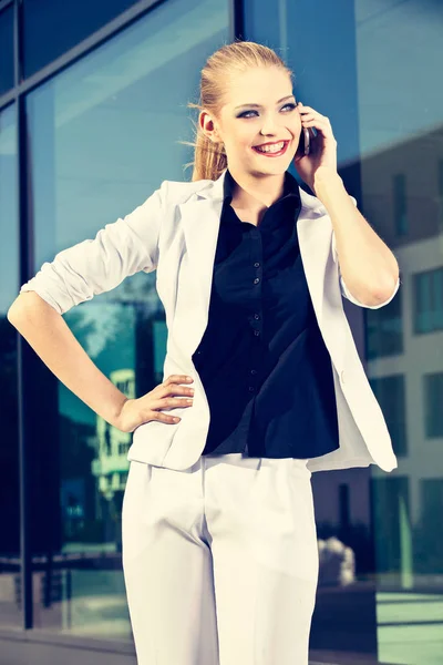 Jonge zakenvrouw praten van een mobiele telefoon op straat tegen gebouw — Stockfoto
