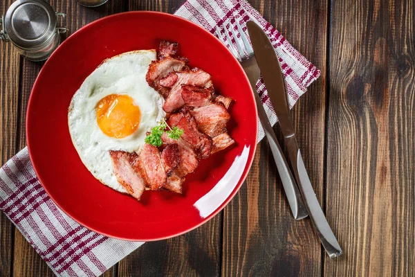 Dilim pastırma füme ve kırmızı bir tabak kızarmış yumurta — Stok fotoğraf
