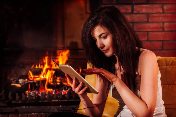 Mujer usando tableta digital sentada junto a la chimenea —  Fotos de Stock