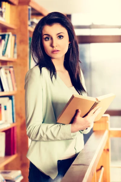 读一本书在书架前面的年轻女人 — 图库照片
