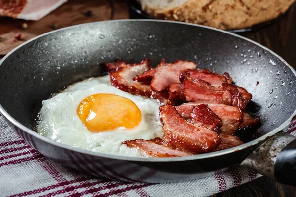 Sneetjes gerookte bacon en gebakken ei in de koekenpan — Stockfoto