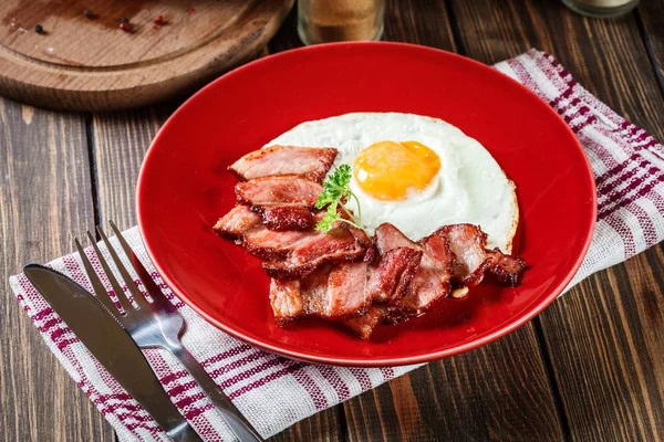 Scheiben geräucherter Speck und Spiegelei auf einem roten Teller — Stockfoto