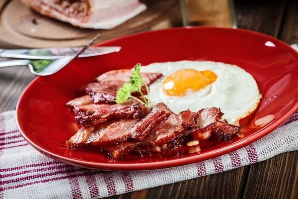 Sneetjes gerookte bacon en gebakken ei op een rode plaat — Stockfoto