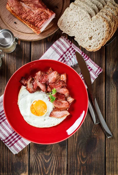 Plátky uzenou slaninou a sázeným vejcem na červené desce — Stock fotografie