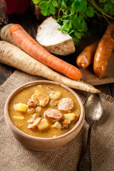 Cuenco de madera de sopa de guisantes partida con salchichas y papas —  Fotos de Stock