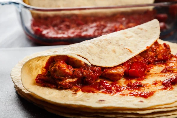 Подготовка традиционных мексиканских энчилад с куриным мясом, острым томатным соусом и сыром — стоковое фото