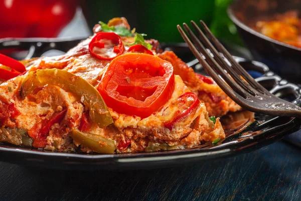 Portion de frittata aux œufs, chorizo à la saucisse, poivron rouge, poivron vert, tomates, fromage et chili dans une assiette sur une table en bois . — Photo