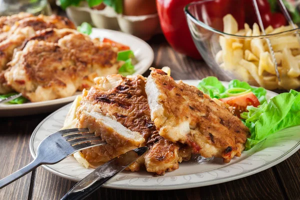 Medalhões de frango com pimentas vermelhas servidas com batatas fritas — Fotografia de Stock