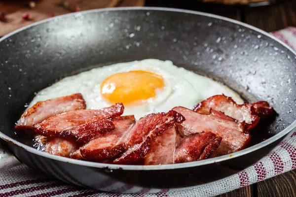 Slices of smoked bacon and fried egg in frying pan — Stock Photo, Image