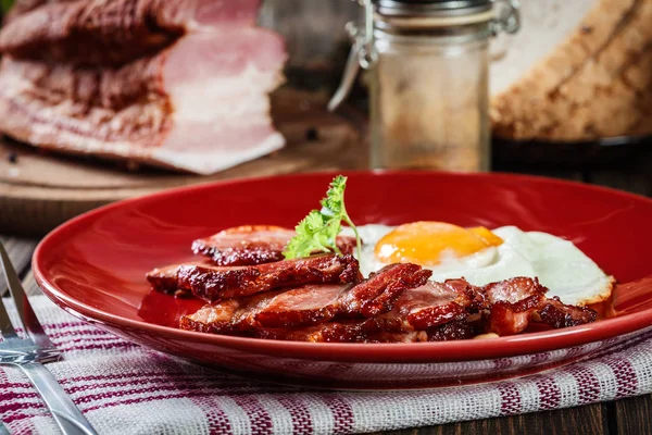 Fatias de bacon defumado e ovo frito em uma placa vermelha — Fotografia de Stock