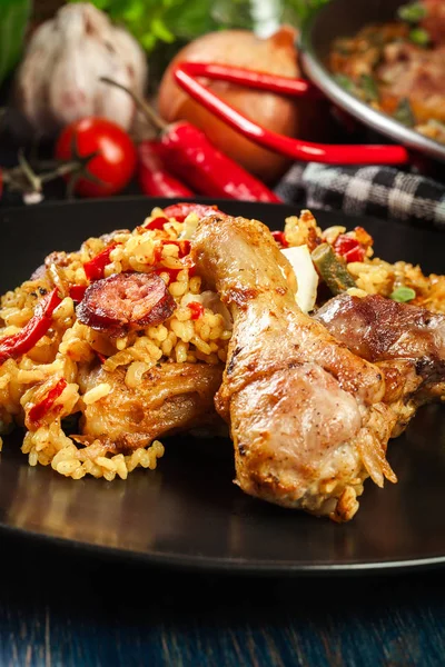 Paella tradizionale con cosce di pollo, chorizo di salsiccia e verdure servite su piatto nero — Foto Stock