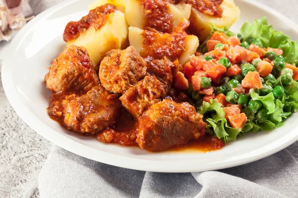 Braised pork meat stew served with potatoes and vegetable salad on a plate