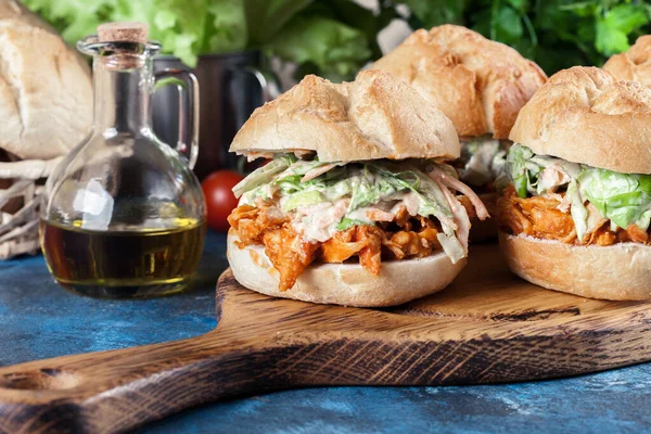 Pulled chicken sandwich with salad and bbq sauce on cutting board