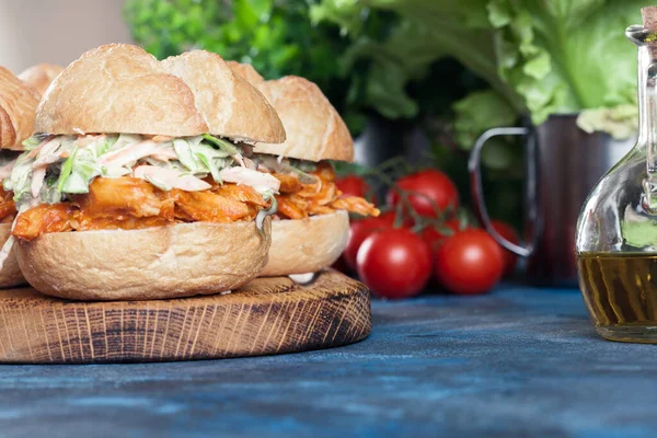 Pulled chicken sandwich with salad and bbq sauce on cutting board