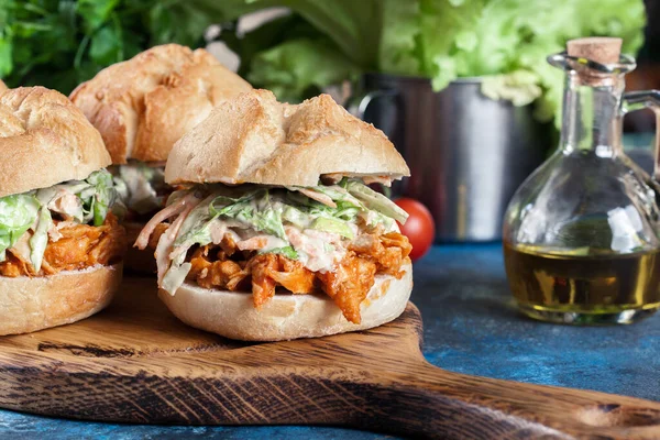 Pulled chicken sandwich with salad and bbq sauce on cutting board