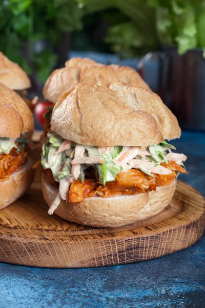 Pulled chicken sandwich with salad and bbq sauce on cutting board