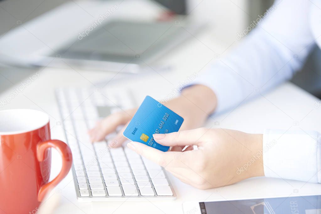 Close-up shot of a young businesswoman sitting in the office in front of computer and holding credit card while typing data.