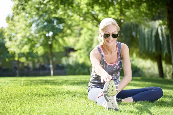 Mulher sentada no parque e alongamento — Fotografia de Stock