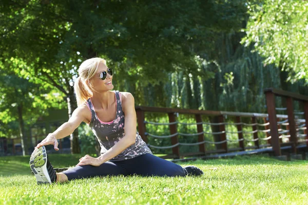 Vrouw zit in het park en stretching — Stockfoto