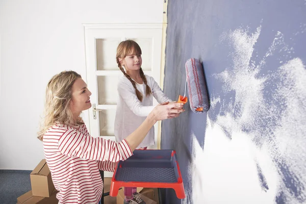 Дочь рисует стену в то время как ее мать — стоковое фото