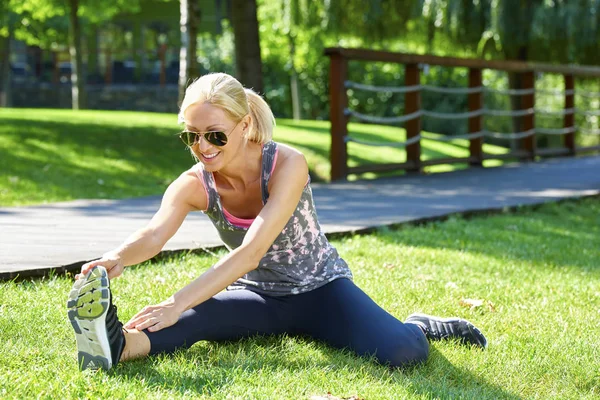 Vrouw zit in het park en stretching — Stockfoto