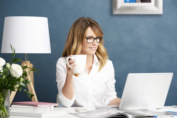 Kvinna som dricker te medan du sitter vid skrivbord — Stockfoto