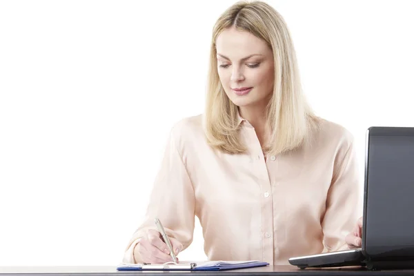 Frau schreibt etwas während sie am Schreibtisch sitzt — Stockfoto