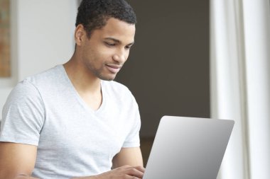 Genç adam laptopunu kullanıyor.