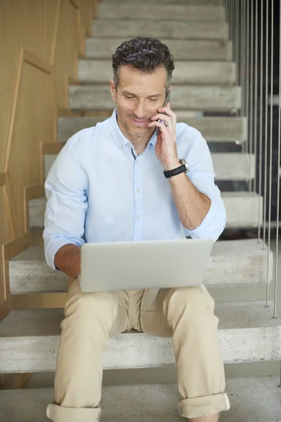 Homem fazendo chamada e usando seu laptop — Fotografia de Stock