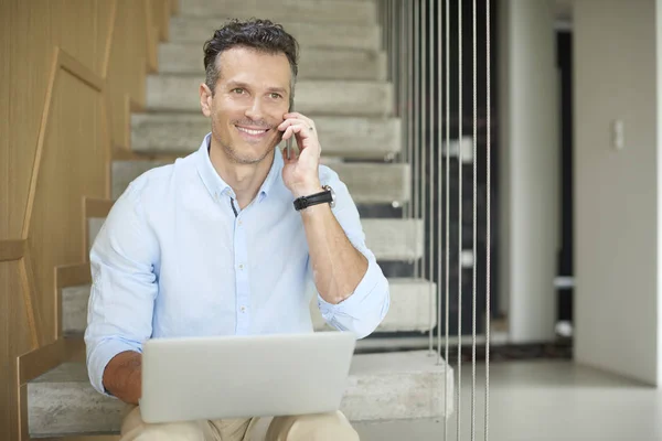 Homem fazendo chamada e usando seu laptop — Fotografia de Stock