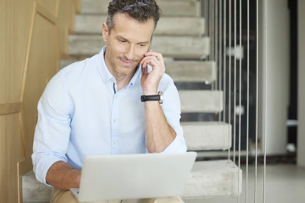 Hombre haciendo llamada y usando su portátil — Foto de Stock