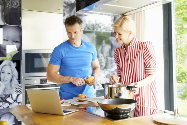 Pareja usando el ordenador portátil mientras cocina —  Fotos de Stock