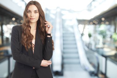 Mağaza önünde yürüyen merdiven dururken güvenle gülümseyen genç bir kadın.