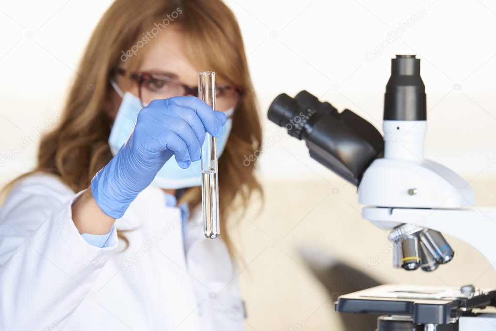 An executive middle aged medical assistant preparing for medical lab test while sitting in front of microscope.