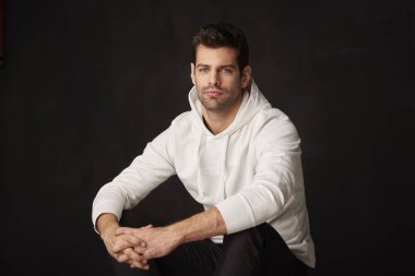 Yakışıklı genç bir adam koyu arka planı süre kameraya bakıyor ve gülümsüyor oturan Studio vurdu. 