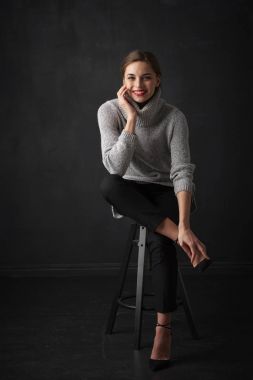 Çekici genç kadın koyu arka plan oturma ve rahatlatıcı boğazlı kazak giyen tam uzunlukta vurdu. 