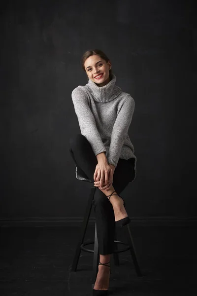 어두운 배경에서 앉아서 스웨터를 매력적인 여자의 — 스톡 사진