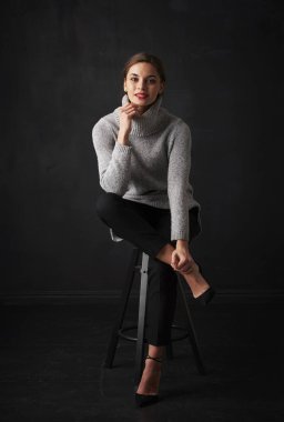 Çekici genç kadın koyu arka plan oturma ve rahatlatıcı boğazlı kazak giyen tam uzunlukta vurdu. 