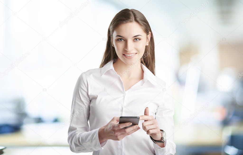 Young businesswoman standing at the office and text messaging before starting business meeting. 
