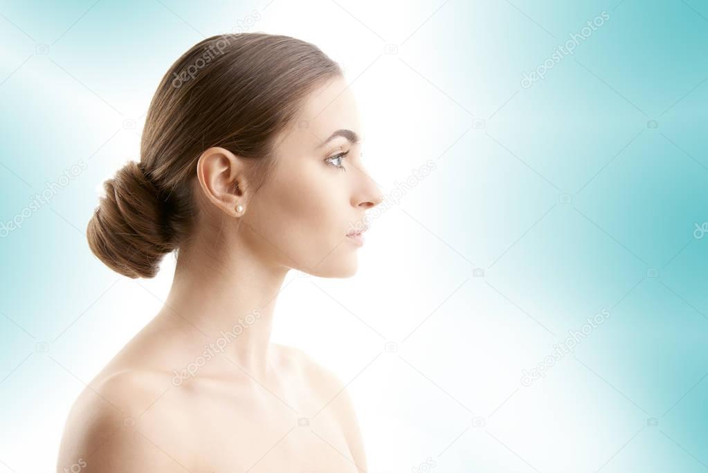 Woman face profile shot. Beautiful young woman with perfect skin looking away while standing at isolated light blue background. 
