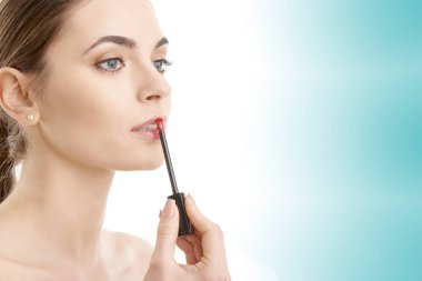 Genç bir kadın pembe ruj izole açık mavi renkli, karşı duran bir aplikatör ile uygulama. 