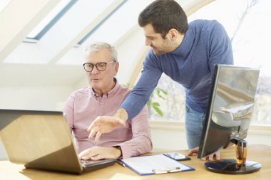 Ofis Masası onun genç asistanı iş adamı onun yanındaduruyor ve yeni proje hakkında danışmanlık bilgisayar önünde oturan üst düzey iş adamı. Ofiste takım çalışması. 