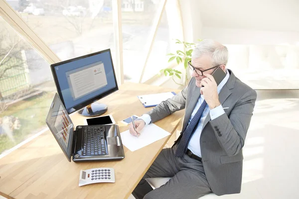 高级理财顾问的高角度拍摄穿着西装 而坐在办公桌前的笔记本电脑和打电话 — 图库照片
